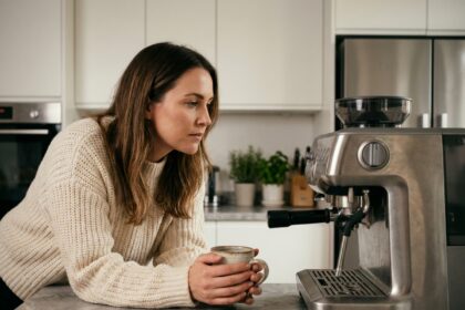 Femme examinant une machine à café expresso dans une cuisine moderne en marbre blanc, tenant un mug en céramique